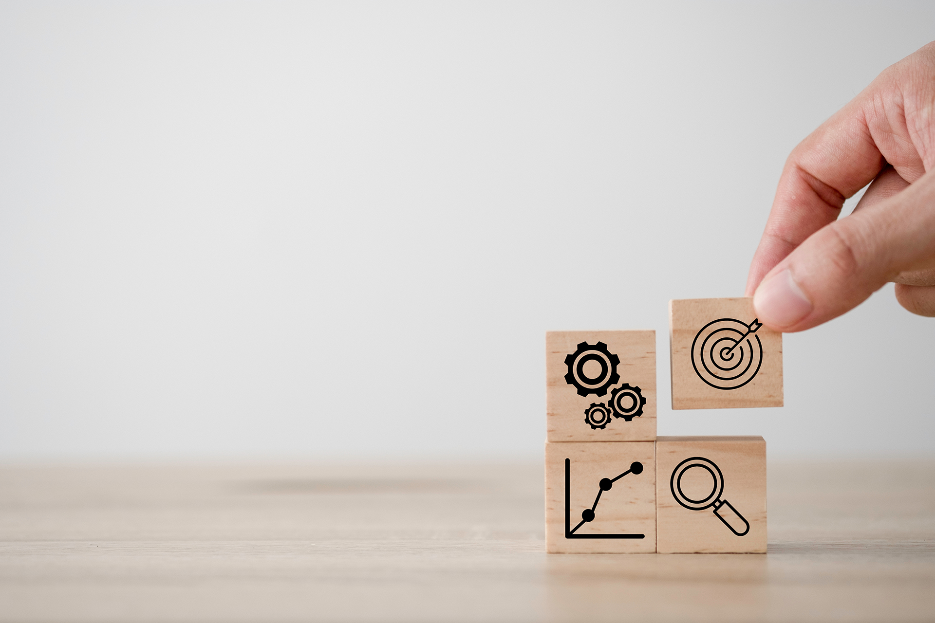 wooden blocks with gears, graph, target, and magnifying glass on them being stack into a square