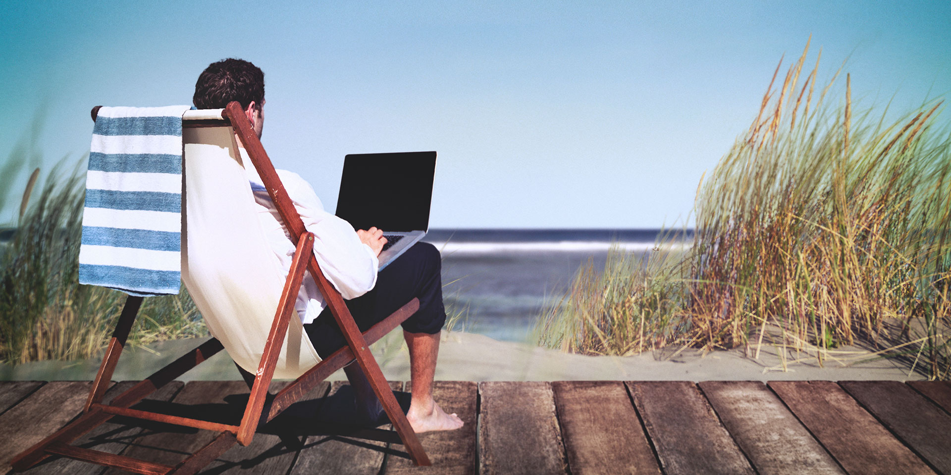 man sitting in a chair on beach looking at laptop